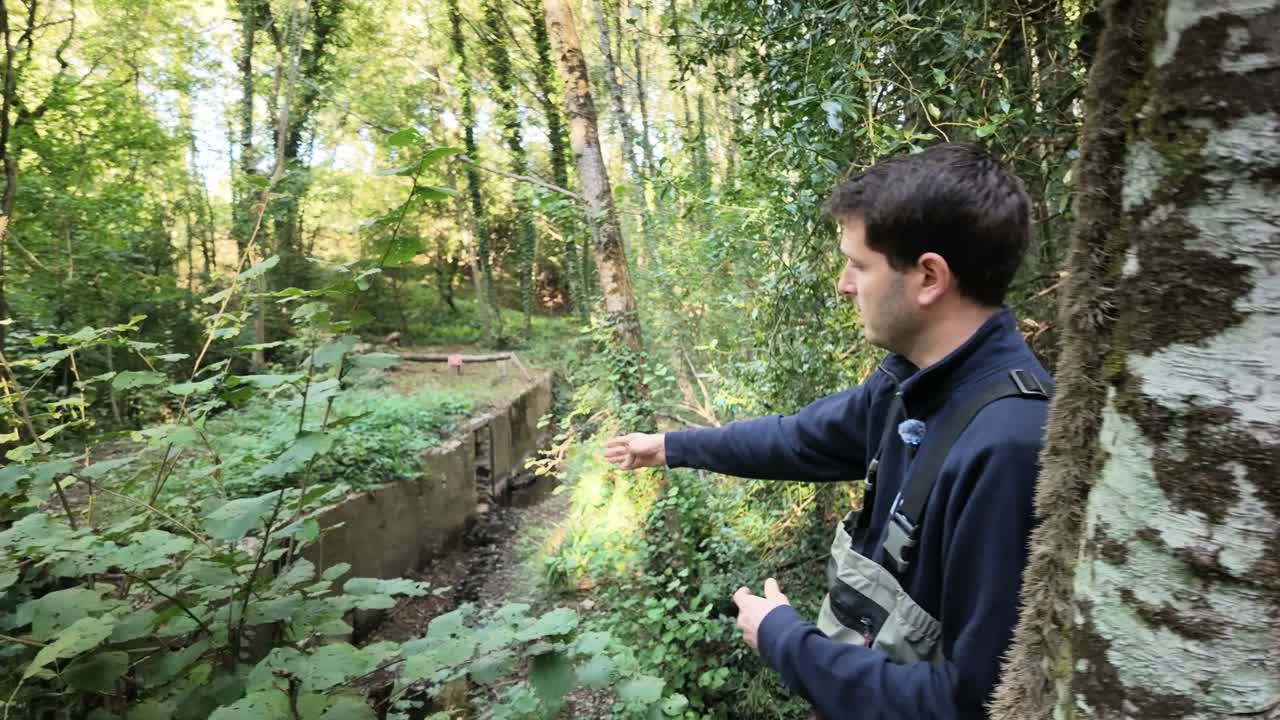 Maxime montre les aménagements du seuil de l’ancien moulin au milieu de la végétation