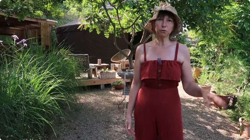 Cécile présente le jardin d’essai, avec la yourte visible derrière elle.